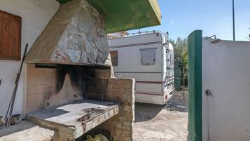 Een buitenkeuken van natuursteen met een barbecue, een tafeltje en een groen zonnescherm.