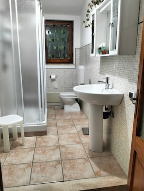 Een badkamer met een douche, toilet, wastafel en een klein krukje.
