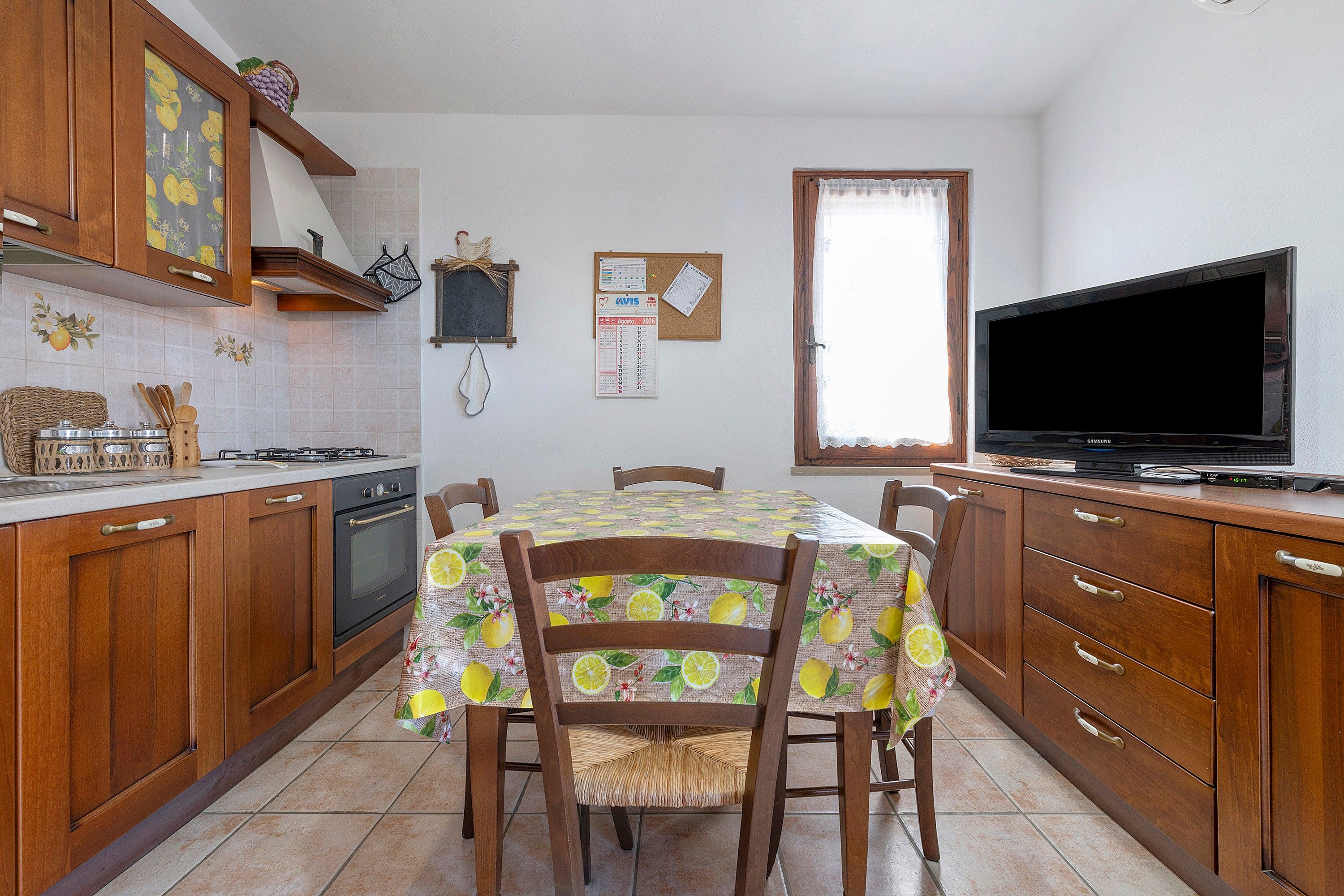 Une cuisine avec des meubles de rangement en bois, une cuisinière à gaz, un réfrigérateur et une table à manger avec des chaises.