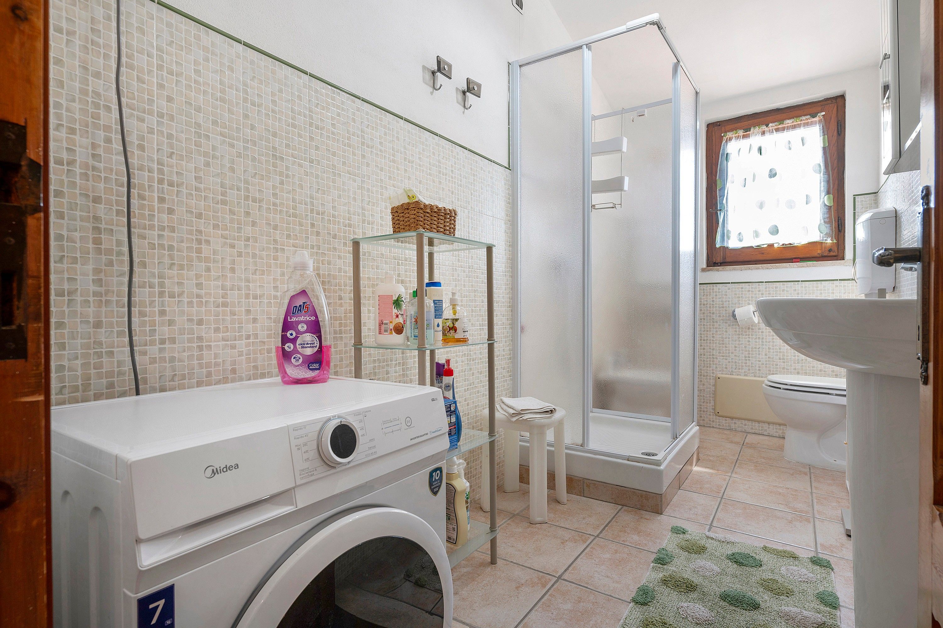 Ein kleines Badezimmer mit Waschmaschine, Duschkabine aus Glas und Fenster mit Blick.
