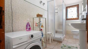 Ein kleines Badezimmer mit Waschmaschine, Duschkabine aus Glas und Fenster mit Blick.