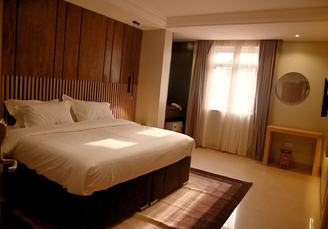 A bedroom with a large bed, wooden paneling on the walls, a bedside table, a mirror, and a window with curtains.