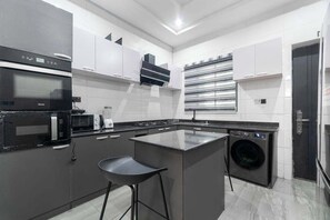 A modern kitchen with a central island, built-in appliances, and a washing machine. - Exclusive Homes By Bomma  (Abuja)