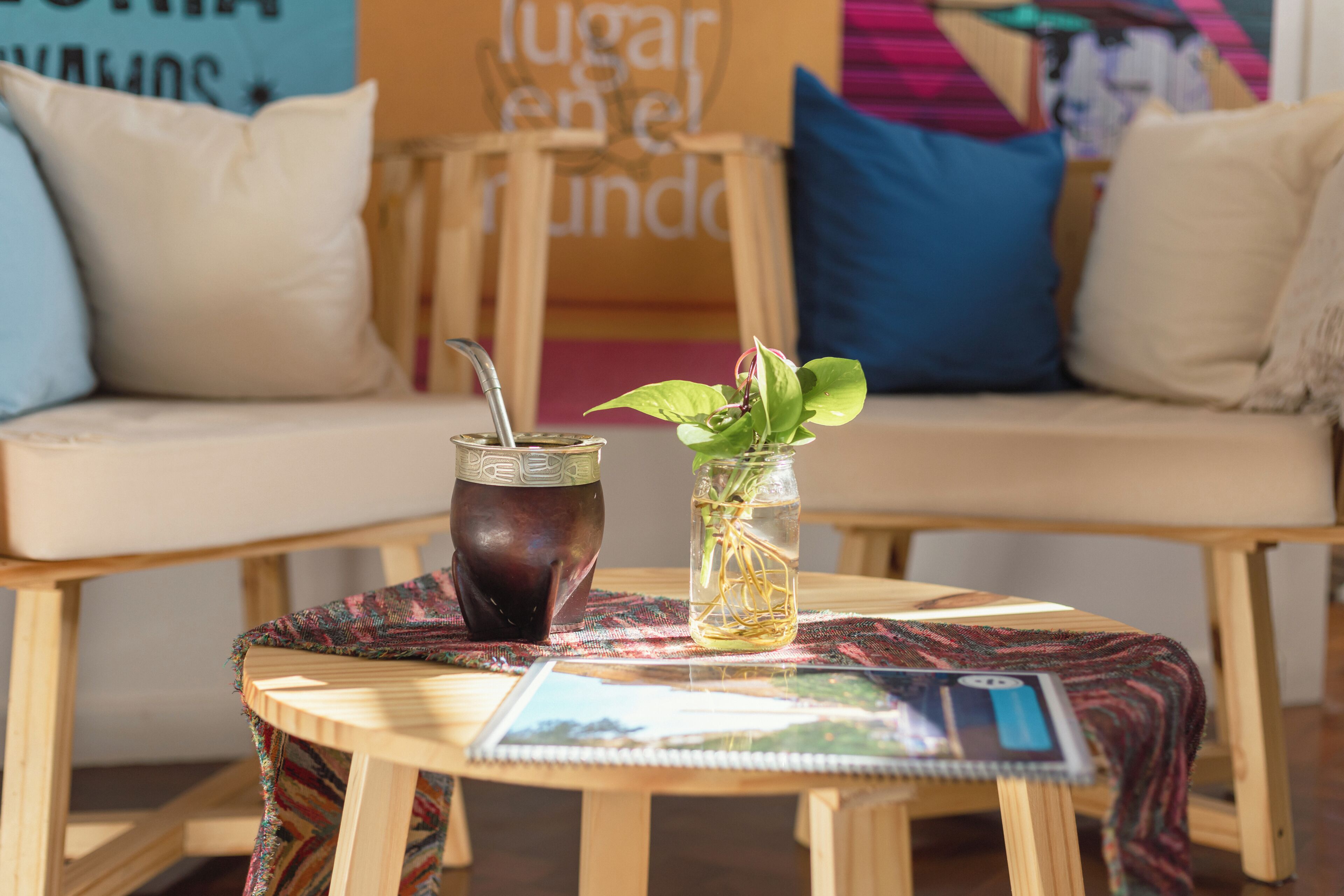 A round wooden table with a notebook, a glass jar with a plant, and a traditional drink container.