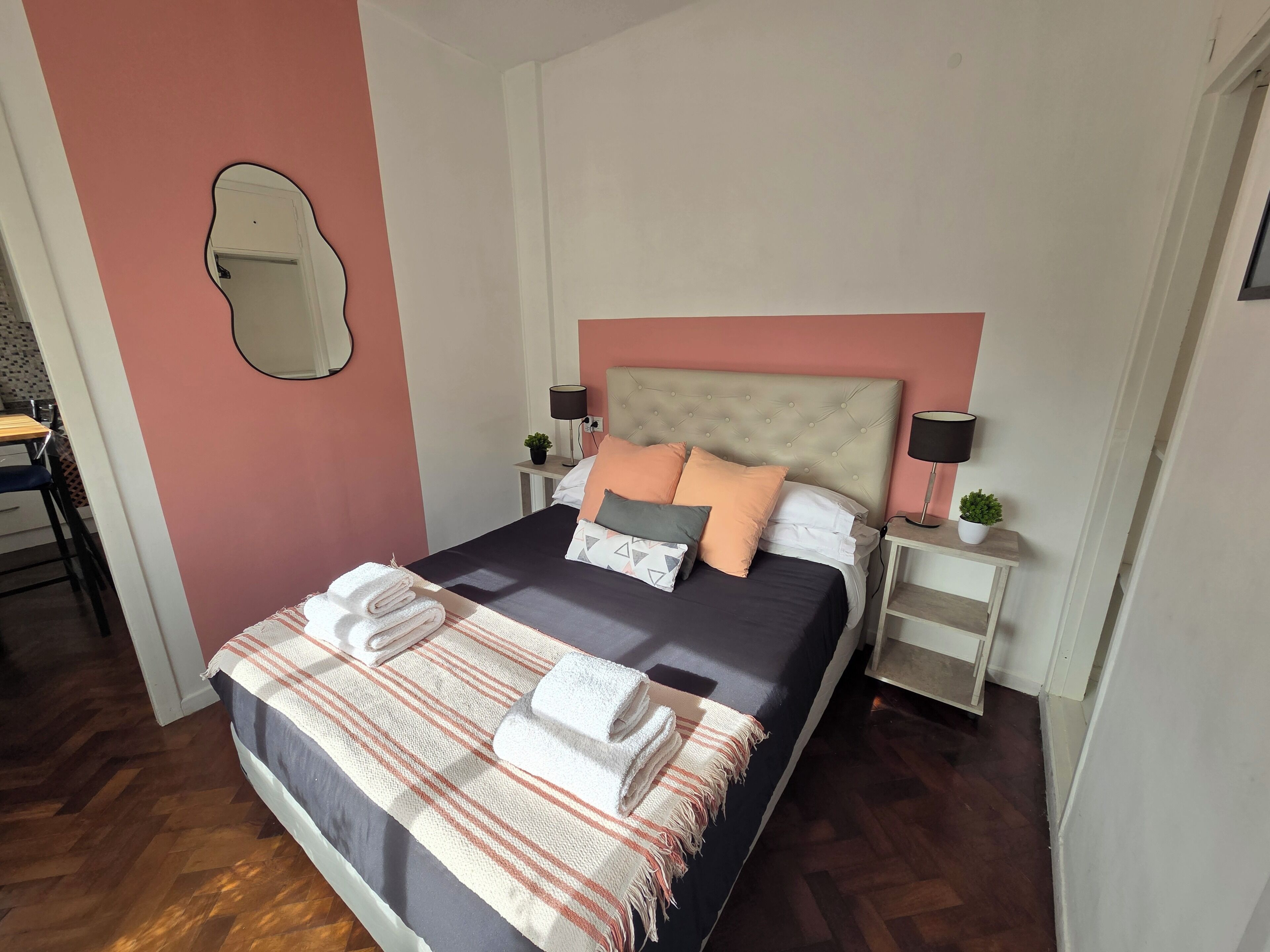 A neatly made bed with pillows and a blanket, a bedside table with a lamp, and a small plant.