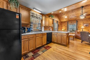 A kitchen with wooden cabinets, a black refrigerator, a coffee maker, and a dishwasher. - Cabin beside Shepherd Creek with Hot Tub and Fire Pit - A World’s Inn Property (Bryson City)