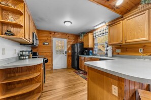 A kitchen with wooden cabinets, a refrigerator, a microwave, and a sink. - Cabin beside Shepherd Creek with Hot Tub and Fire Pit - A World’s Inn Property (Bryson City)