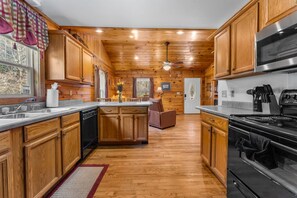 A cabin-style kitchen with wooden cabinets, a central island, a microwave, and a stove. - Cabin beside Shepherd Creek with Hot Tub and Fire Pit - A World’s Inn Property (Bryson City)