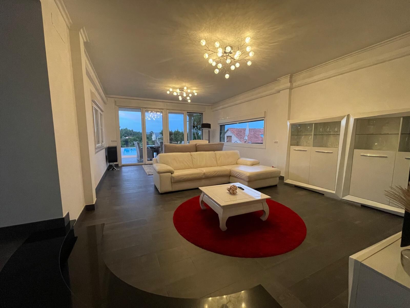Een moderne woonkamer met een bank, een salontafel en een rood vloerkleed. Er is een groot raam met uitzicht op het landschap.