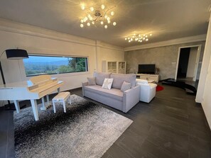 A modern living room with a sofa, a TV, a desk, and a large window.