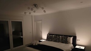 Quarto com cama, mesas de cabeceira, luminária no teto e porta deslizante.