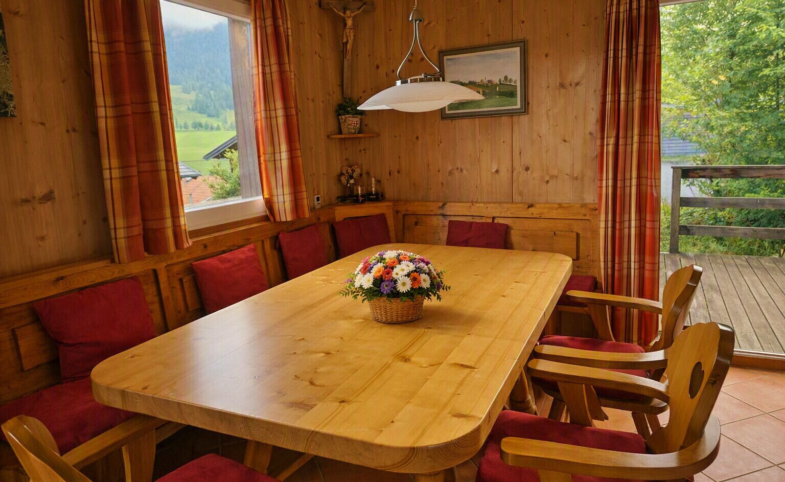 Een houten eettafel met een bloemstuk in het midden, omringd door rode, beklede stoelen.