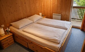Une chambre aux murs lambrissés, avec un lit double, des tables de chevet, une lampe et une fenêtre donnant sur un beau paysage.