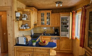 Eine Holzhütte mit einer Kücheninsel, eingebauten Schränken und einem Fenster mit Karomustertvorhängen.