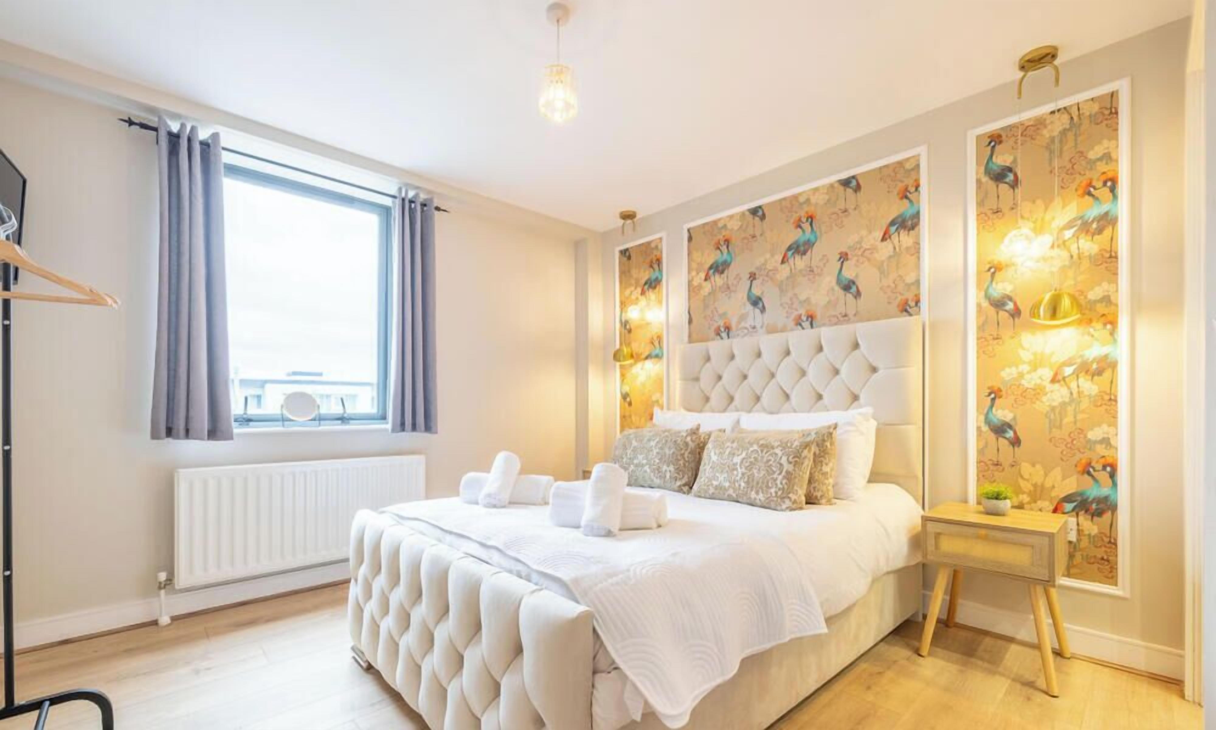 A bedroom with a large bed, a radiator, a window with curtains, and a wall with a bird-themed wallpaper.