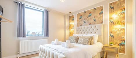 A bedroom with a large bed, a radiator, a window with curtains, and a wall with a bird-themed wallpaper.