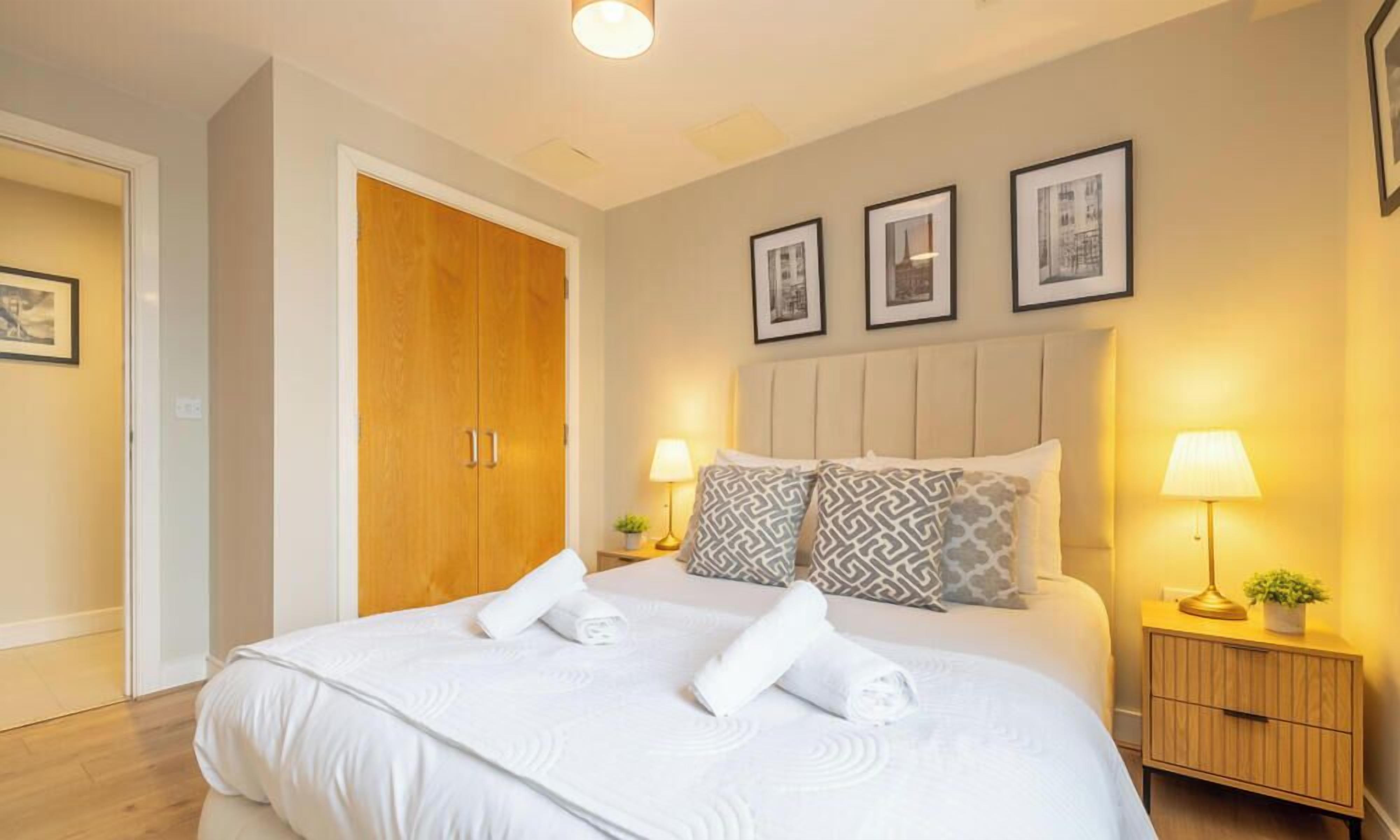 A hotel room with a large bed, two bedside lamps, a wooden wardrobe, and three framed pictures on the wall.