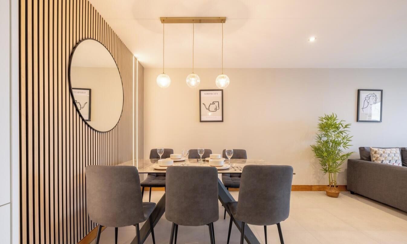 A modern dining area with a round table, grey chairs, and hanging pendant lights.