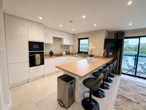 A modern kitchen with a central island, bar stools, and a view of the outdoors. - Belfast Quarters: Riverside (Belfast)