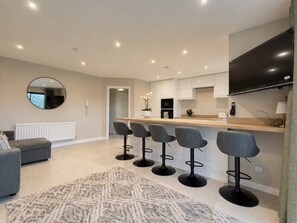 A modern kitchen with a bar area, a dining table, and a sofa in a living area. - Belfast Quarters: Riverside (Belfast)