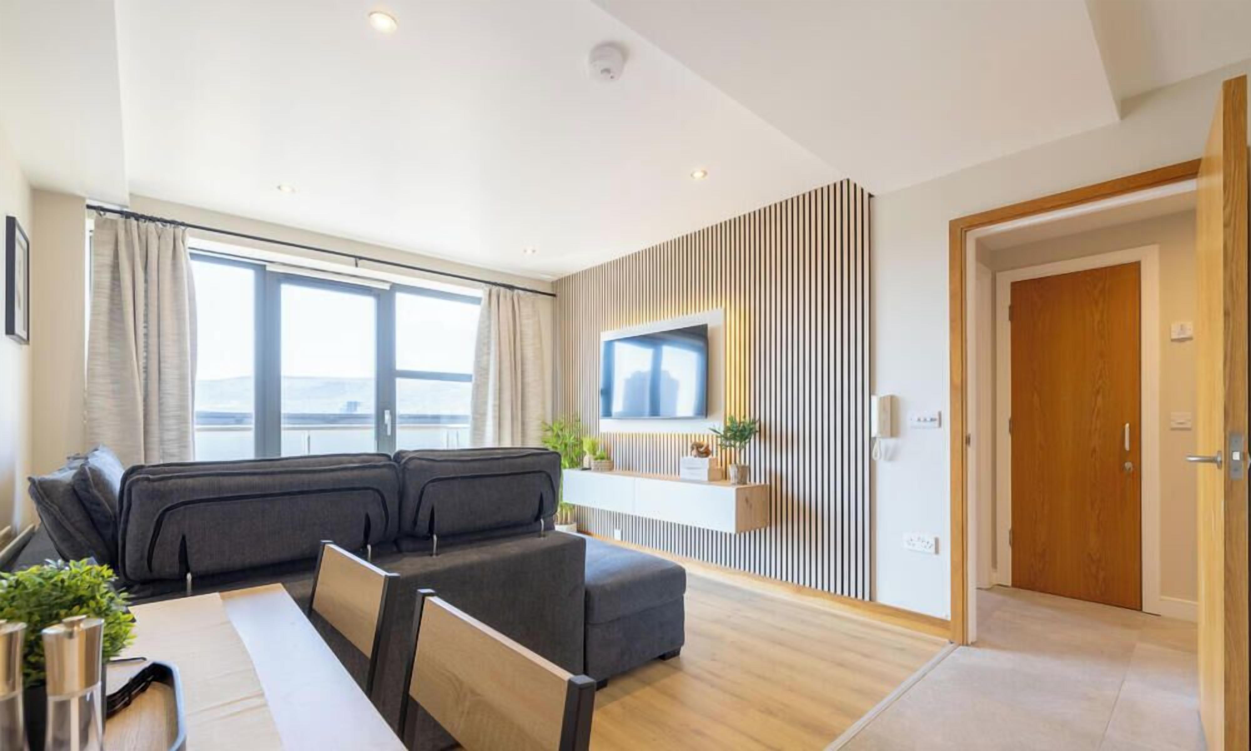 A modern living room with a sofa, a TV mounted on a wall, and a wooden door.