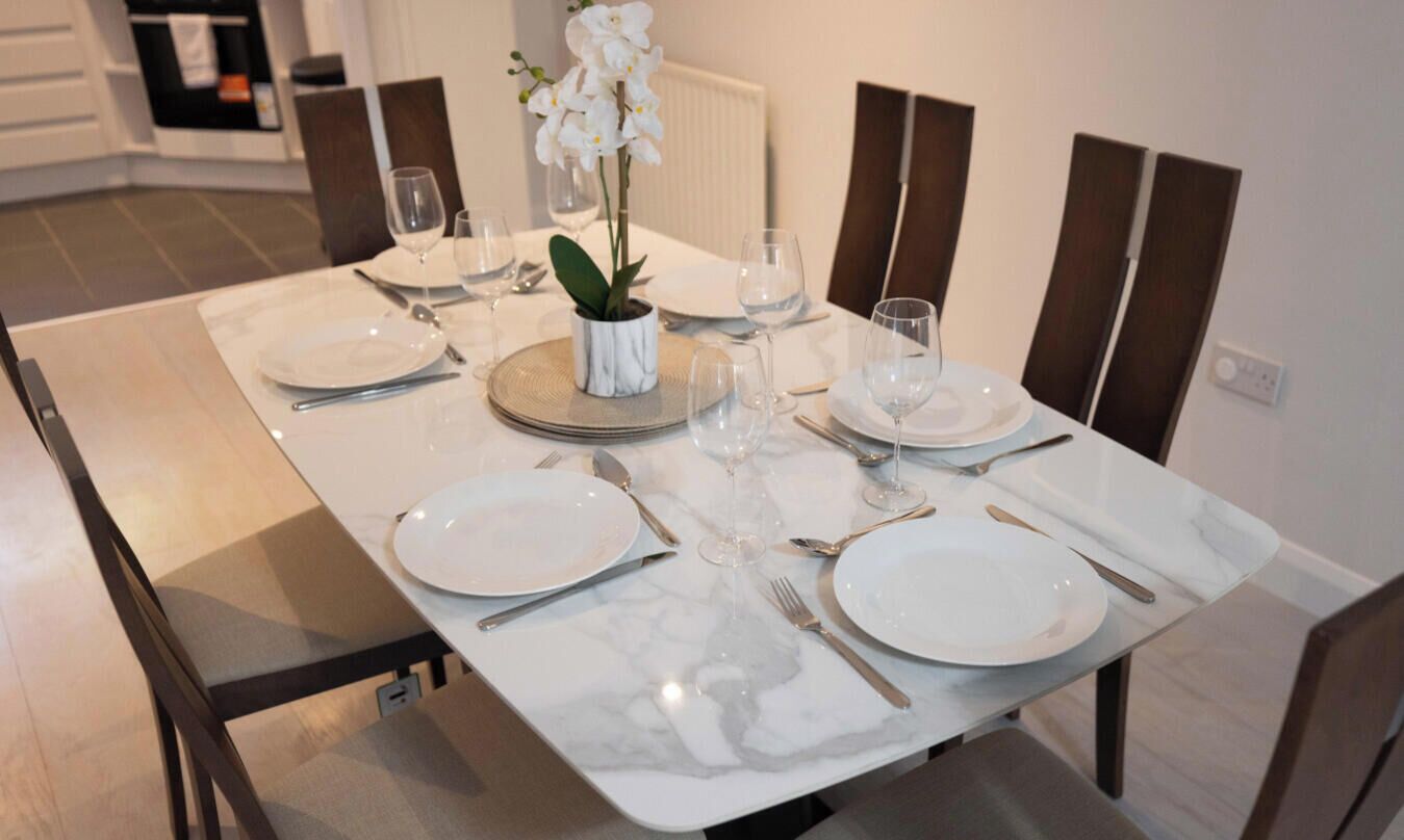 A dining table set with plates, cutlery, and glasses, with a potted orchid centerpiece.