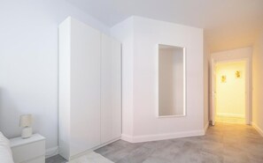 A modern, minimalist room with a built-in wardrobe, a bedside table with a lamp, and a hallway leading to another room. - Belfast Quarters Lower Windsor (Belfast)