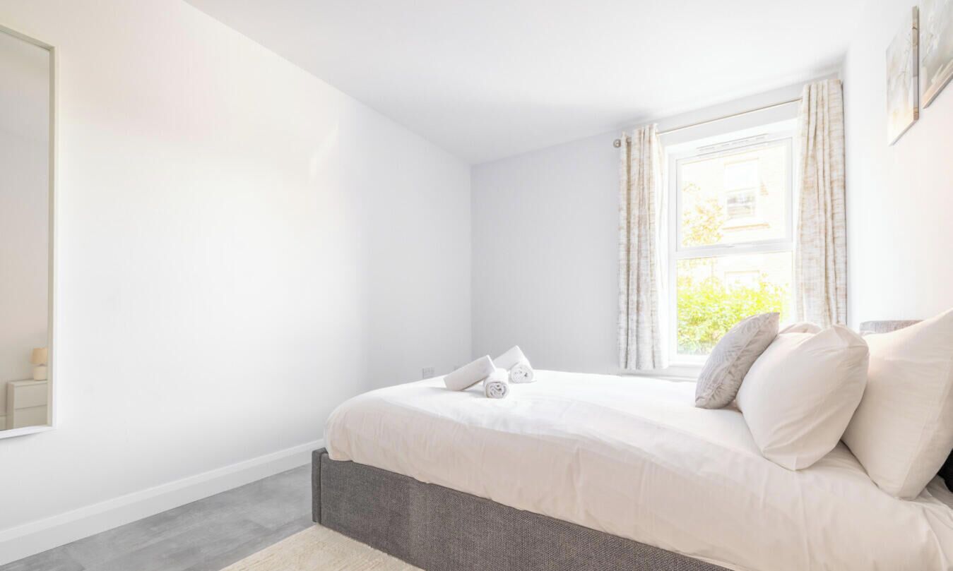 A bedroom with a bed, a window with curtains, and a nightstand.