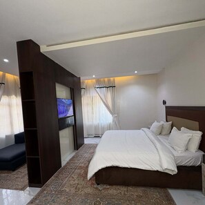 Un dormitorio moderno con una cama grande, un televisor de pantalla plana montado en una pared oscura y una alfombra estampada.