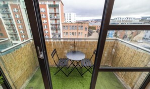 Een balkon met een tafel en stoelen, uitzicht op een stadsgezicht en een bamboescherm.