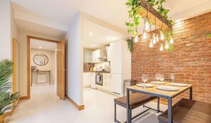 A modern kitchen with white cabinets, a brick accent wall, and a dining area with a wooden table and bench. - Belfast Quarters: 5th Floor Gem! (Belfast)