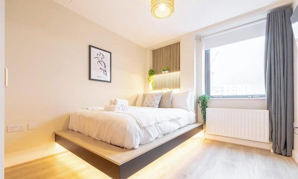 A modern bedroom with a bed, bedside table, and a window with curtains. - Belfast Quarters: 5th Floor Gem! (Belfast)