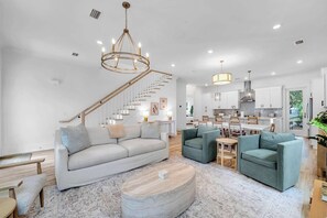 A spacious living area with a sofa, two armchairs, a coffee table, and a staircase leading to an upper level. - Lovely Day 30a by Stay on 30a (Inlet Beach)