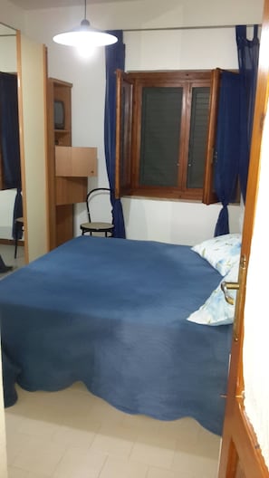 A bedroom with a bed, a chair, a desk, and a window with curtains. - Apartment 'Suite Delle Rose' with Shared Garden, Wi-Fi and Air Conditioning (La Maddalena)