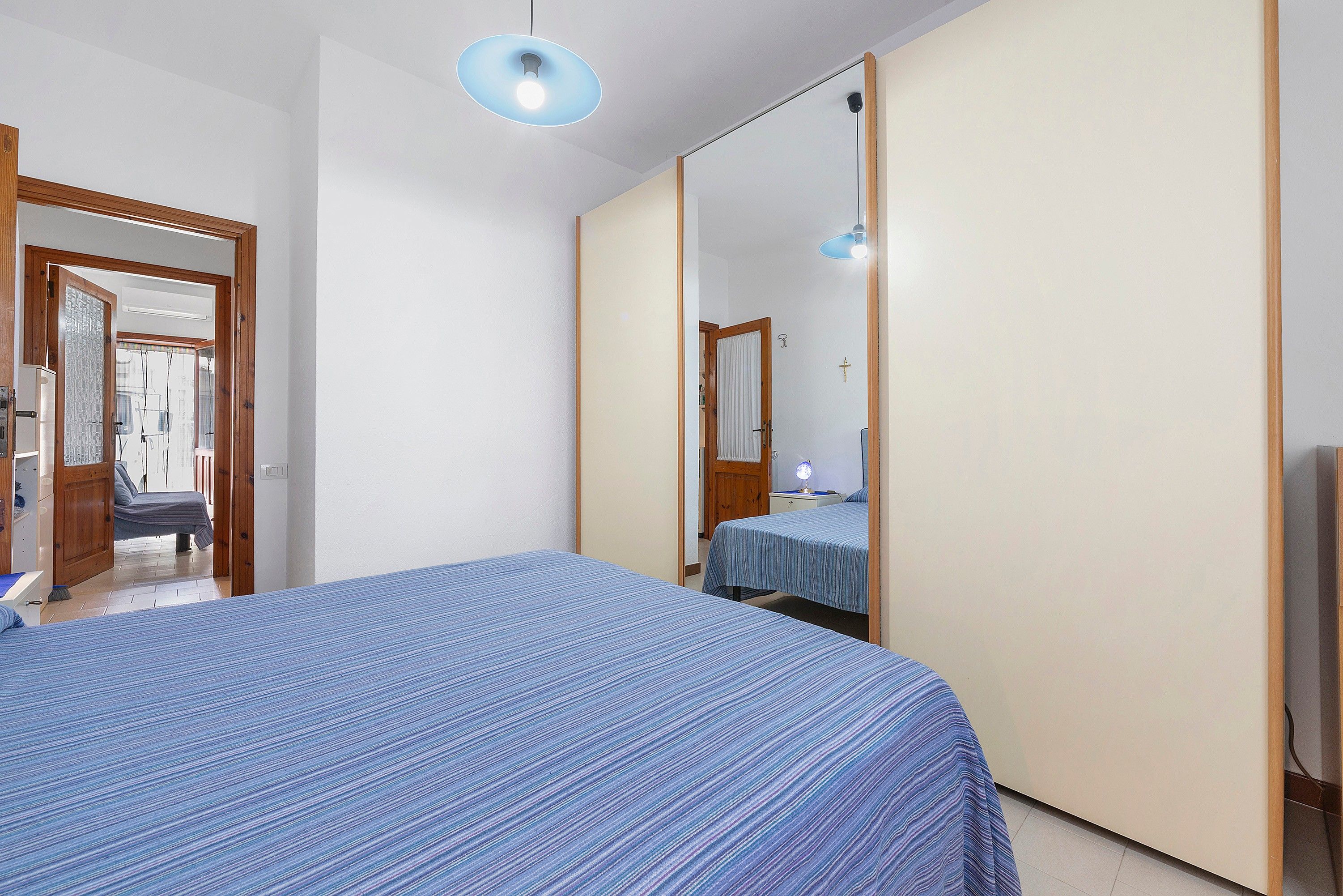 Une chambre à coucher avec un grand lit, une armoire, un miroir et un luminaire au plafond.