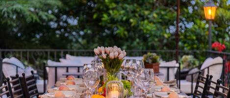 An outdoor dining area with a table set for a meal, surrounded by chairs.