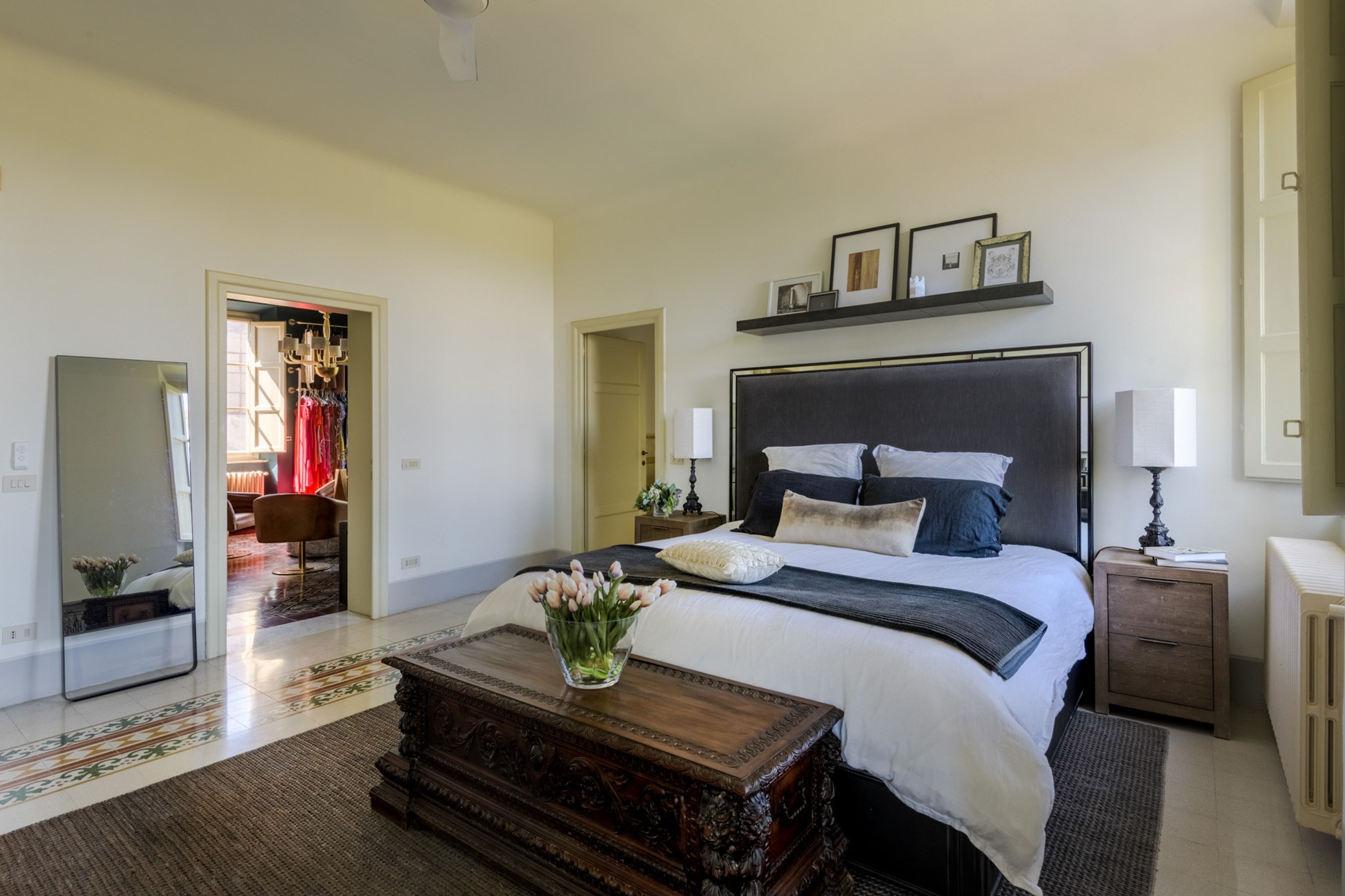 Een slaapkamer met een groot bed, nachtkastjes, een dressoir, een spiegel en een gang naar een kleedruimte.