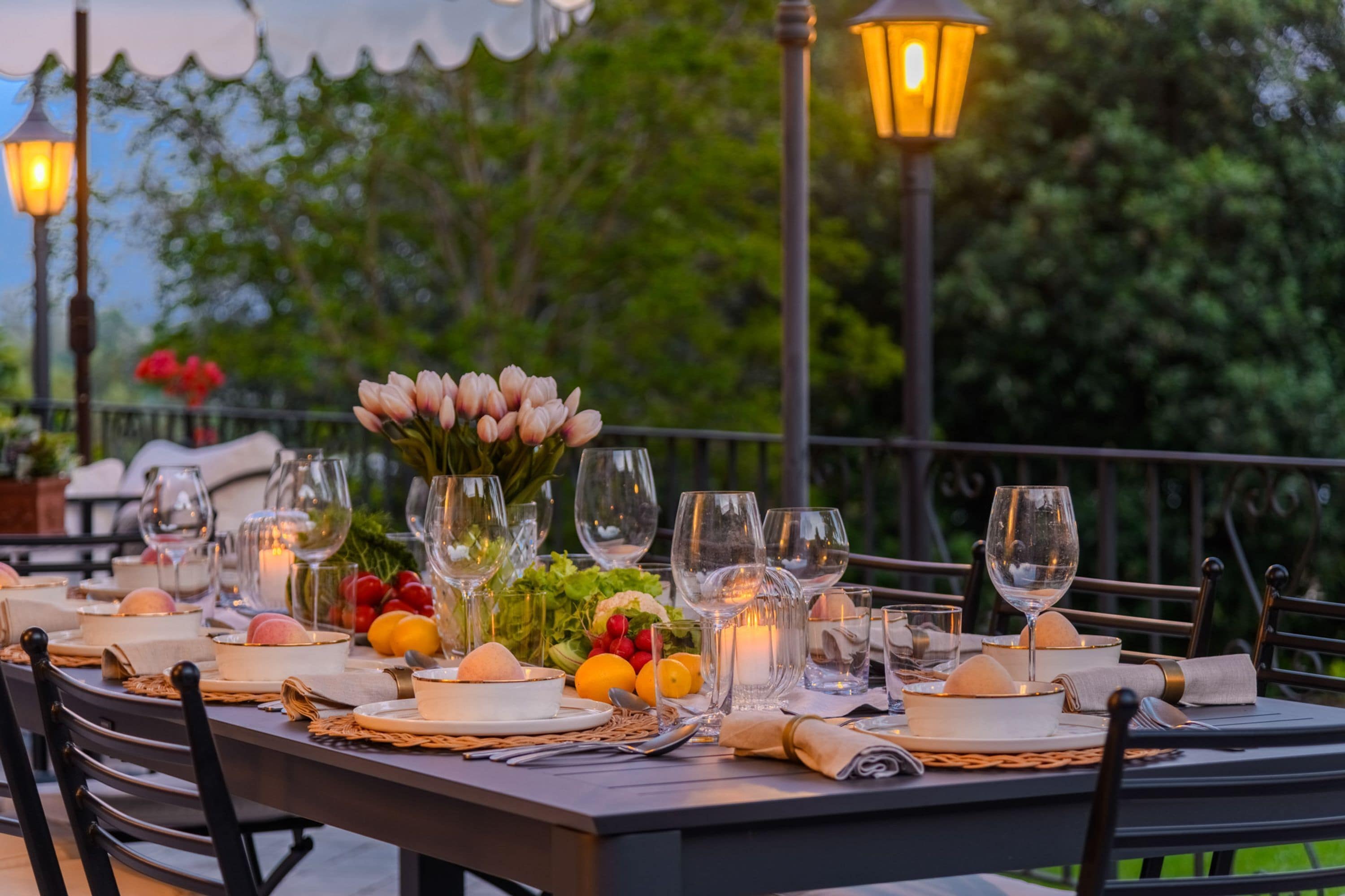 An outdoor dining table set with multiple wine glasses, plates, and a centerpiece of flowers.