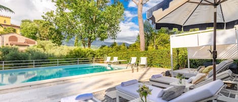 A poolside area with lounge chairs, umbrellas, and a view of a building in the background.