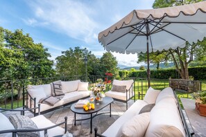An outdoor patio with a sofa set, a round table, and a large umbrella. - Villa Bertolli in Lucca (Lucca)