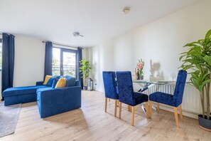 Ein modernes Wohnzimmer mit einem blauen Sofa, einem Esstisch mit Stühlen und einer Zimmerpflanze.