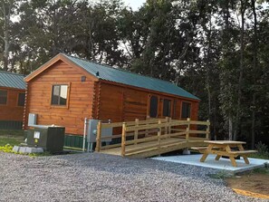 A wooden cabin with a metal roof, a wooden bridge, and a picnic table.