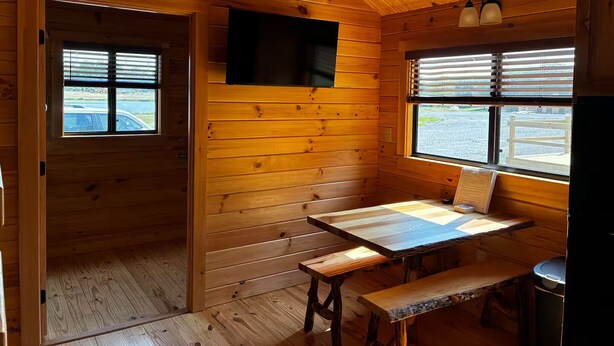 A wooden cabin interior with a wooden table, bench, and a mounted television.