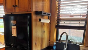 A kitchen with wooden cabinets, a black refrigerator, a stainless steel sink, and a window with blinds.
