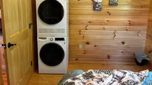 A laundry room with stacked washing machines, wooden walls, and two framed pictures.