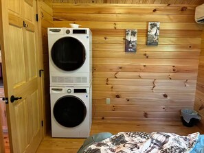 A laundry room with stacked washing machines, wooden walls, and two framed pictures.