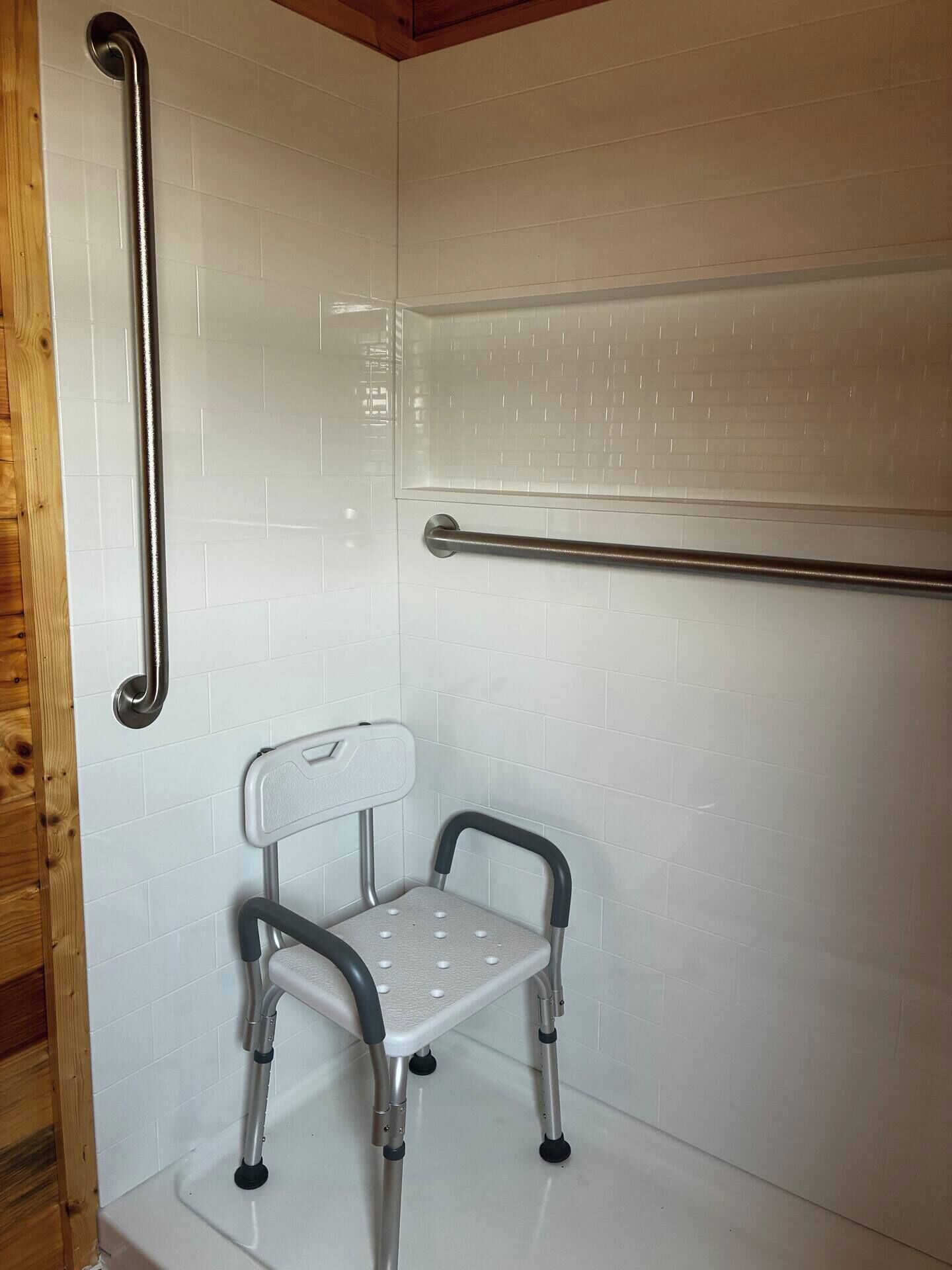 A shower area with a white tiled wall, a metal grab bar, and a mobility aid.