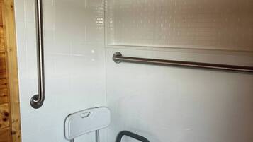 A shower area with a white tiled wall, a metal grab bar, and a mobility aid.
