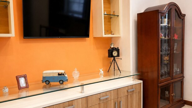 Una sala moderna con un televisor de pantalla plana montado en la pared, un mueble de madera con puertas de cristal y una cámara antigua sobre un trípode.