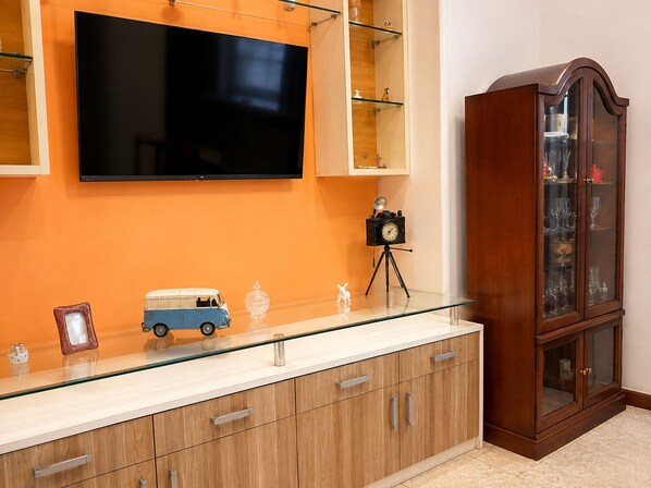 A modern living room with a flat-screen TV mounted on the wall, a wooden cabinet with glass doors, and a vintage camera on a tripod.